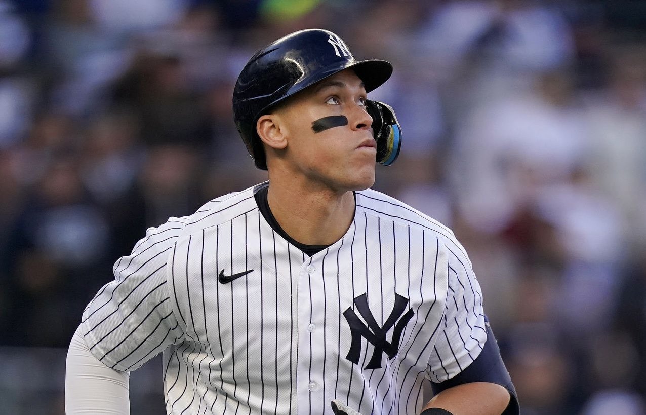 Pelotero de los Yanquis en uniforme de rayas blancas observa el juego desde el banquillo con casco y protector bucal