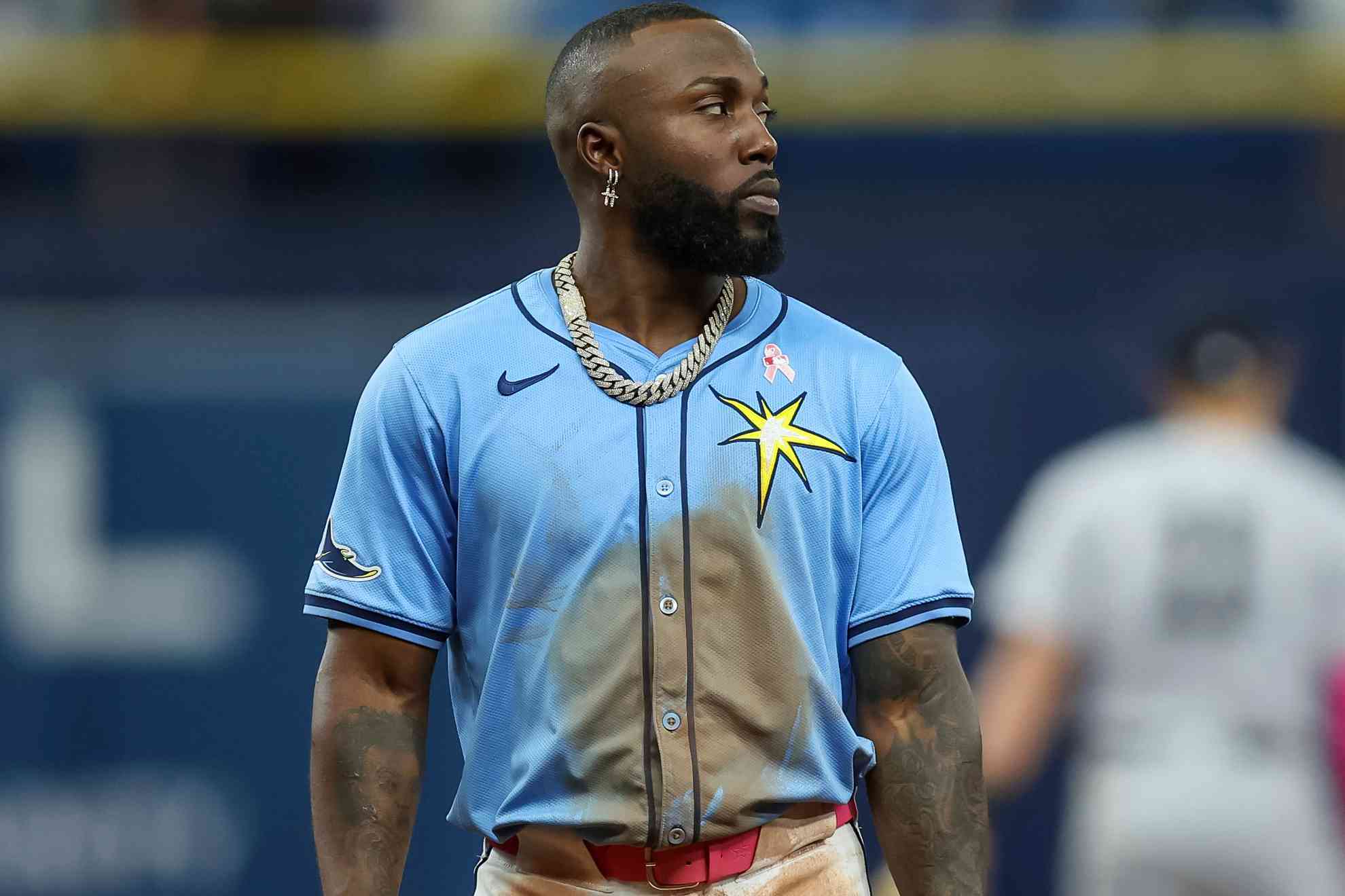 Pelotero con uniforme azul claro de los Rays con estrella amarilla en el pecho, cadena dorada y aretes, durante un partido en el estadio