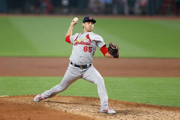 Lanzador de los Cardenales en su movimiento de lanzamiento, uniforme gris de visitante con número 65, en la loma durante un juego