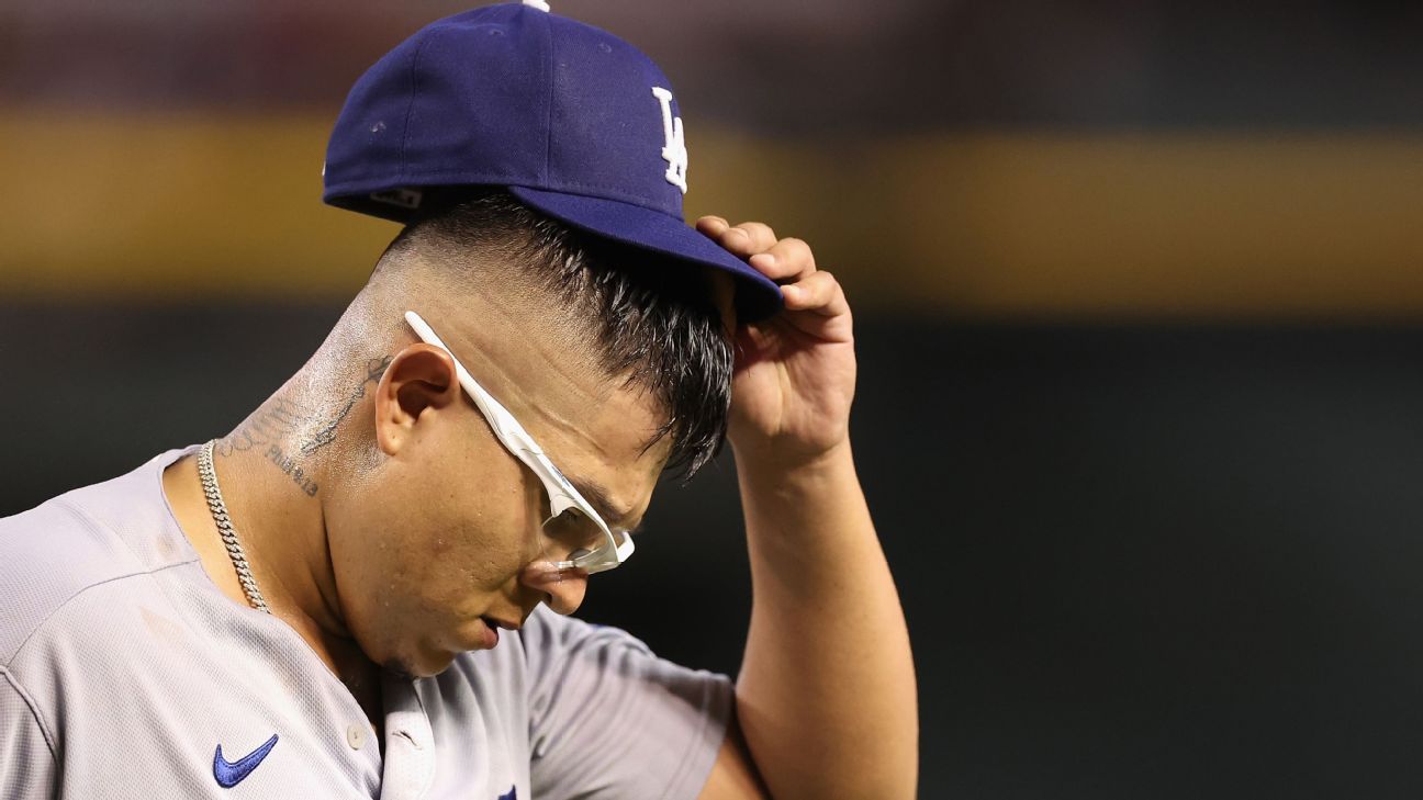 Pelotero de los Dodgers con uniforme gris de visitante, gafas de seguridad y gorra azul, ajustándose la visera durante un partido
