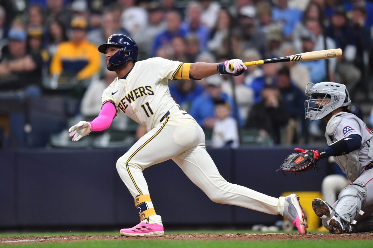 Pelotero número 11 de los Brewers en uniforme crema conecta un batazo durante un juego, con receptor de equipo visitante de fondo