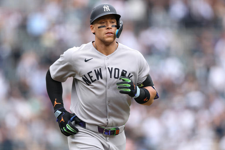 Pelotero de los Yanquis en uniforme gris de visitante corre hacia las bases con guantes de bateo verde y azul