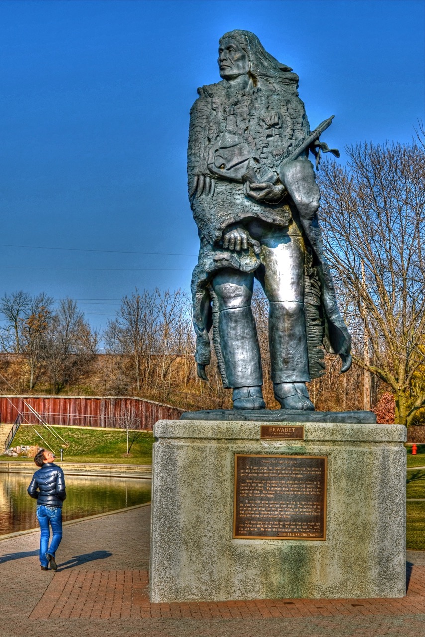 Ēkwabet plaque | Listen, for I speak but once…. As I gaze across the waters of the shimmering Fox River, I see the smoke of thousands of teepees where I once saw only gentle prairies and lush forests abundant with game. Many moons ago my people were among the first voices to be heard in this land. We came to live in peace with nature. We hunted and fished. We married, bore children and died at our appointed time. The bones of my people mingle here with the earth. We loved this Valley. It was with great sadness that we had to leave our home. We were few, and the settlers were many. The spirits of my ancestors have never left this great Valley, and occasionally, you may glimpse our shadows or feel our presence as we tread silently along the shores of our beloved Fox River. Our final prayer as we left our land was that you would love this Valley as much as we loved it. We were one with the earth, sky and water. We were the Neshnabek, the “People” of the Valley.