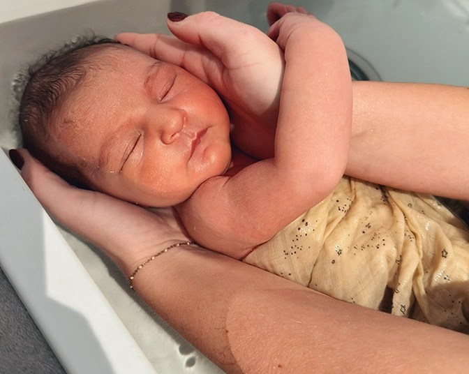 Nouveau-né enveloppé dans un drap, soutenu par la tête dans une petite baignoire