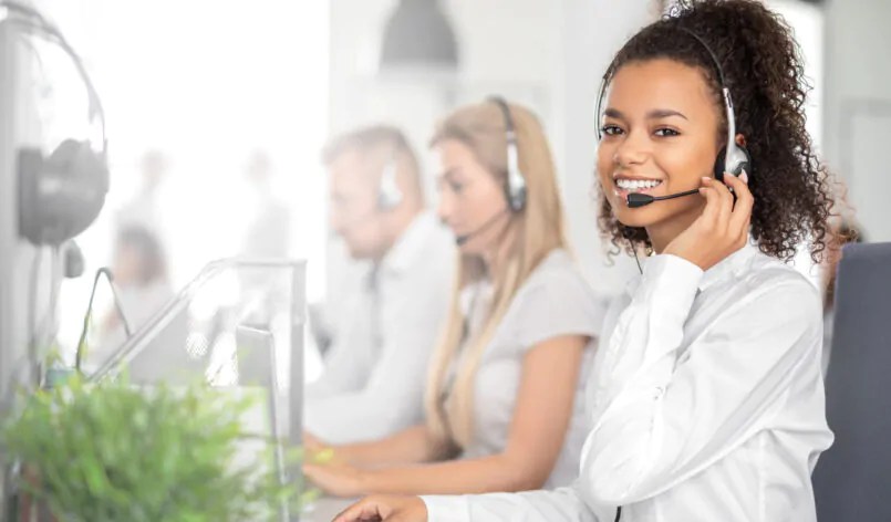 Call center worker accompanied by her team. Smiling customer support operator at work. Young employee working with a headset.