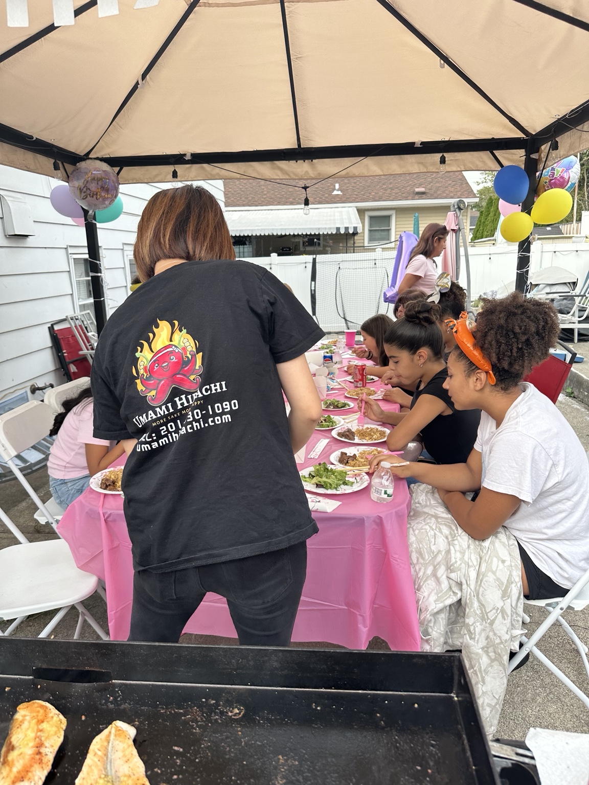 Guests enjoying a hibachi dinner at a pink-covered table beneath a patio gazebo