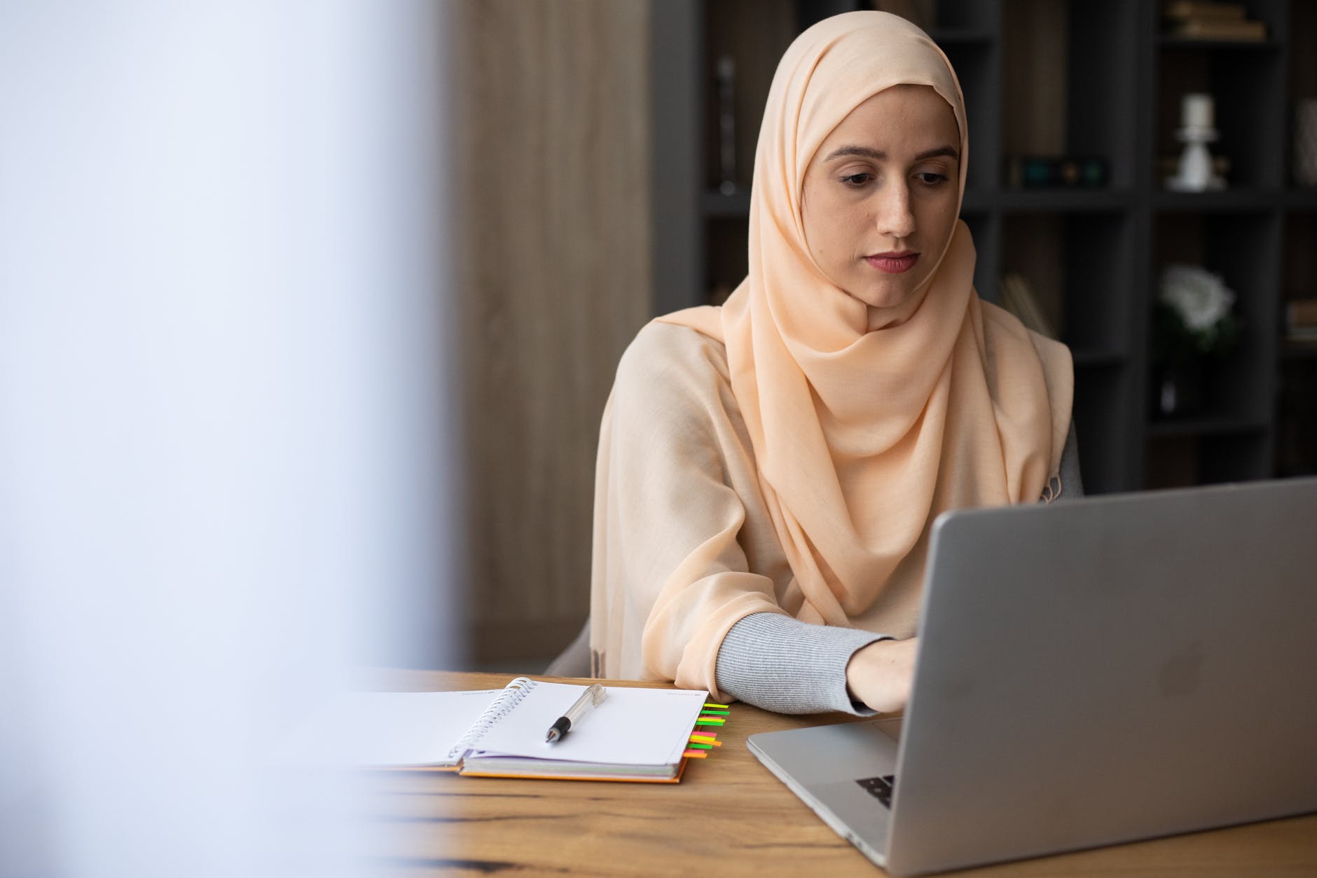 focused muslim woman in hijab sitting at table with laptop and organizer