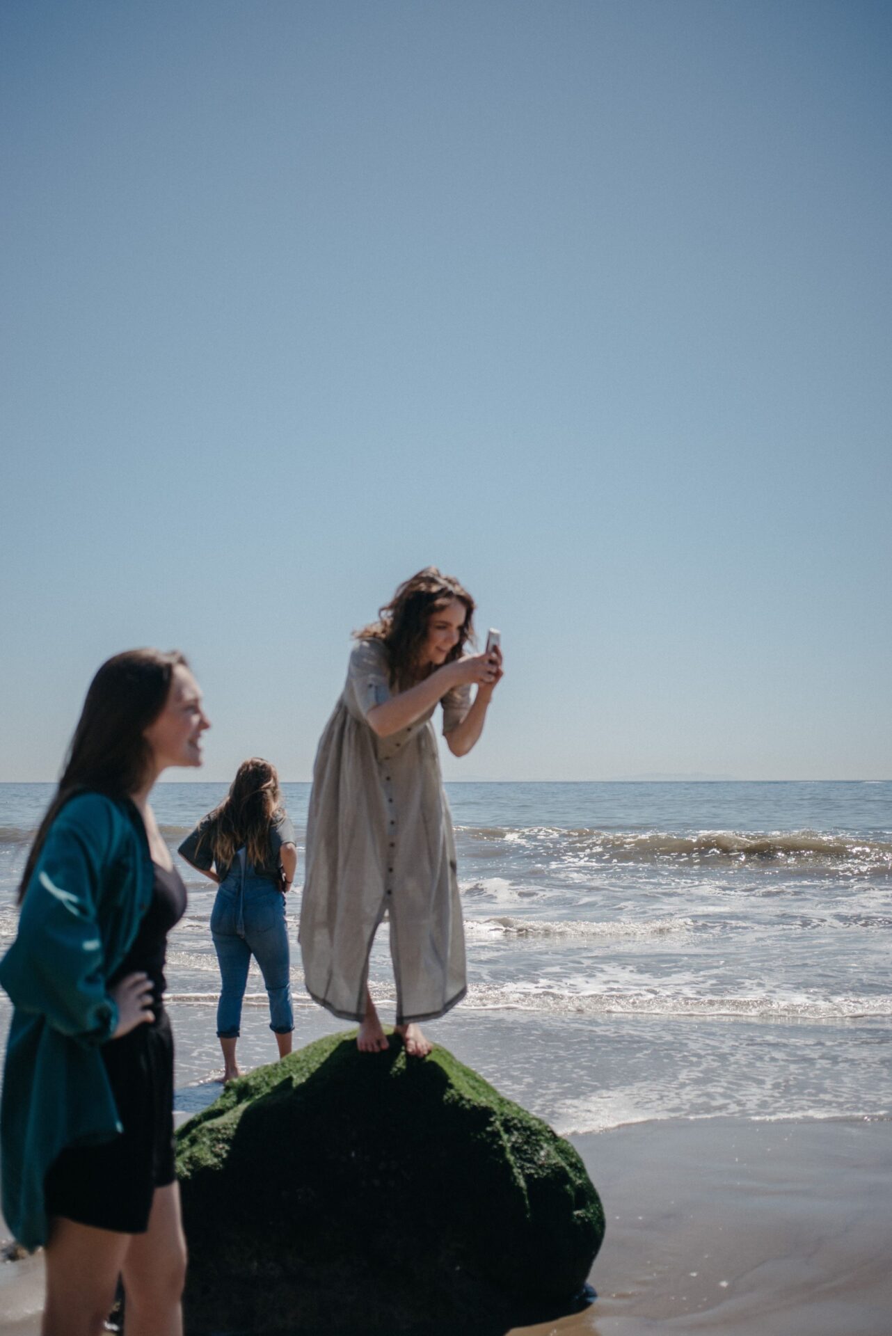 Katelyn Pons Standing on a rock on the beach while taking a photo on her phone