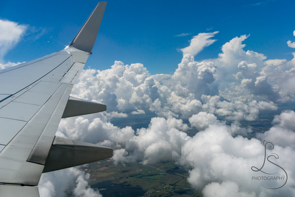 Puffy clouds floating by our airplane's wing | BIG tiny World Travel