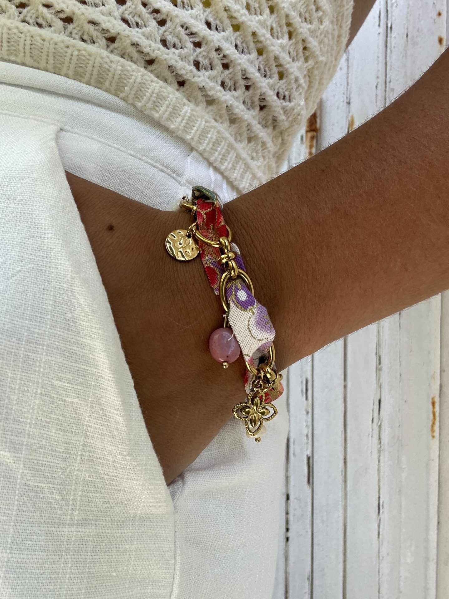 Bracelet Pétillante porté, ruban fleurie et breloques aux tons rosés