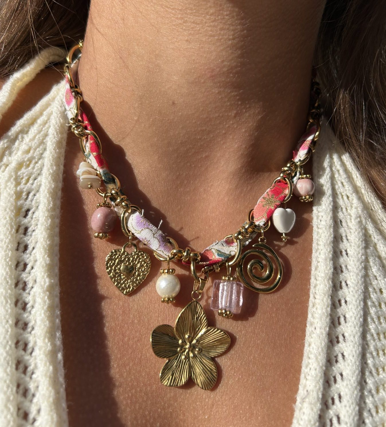 Collier Pétillante porté, ruban fleuri et breloques aux tons rosés