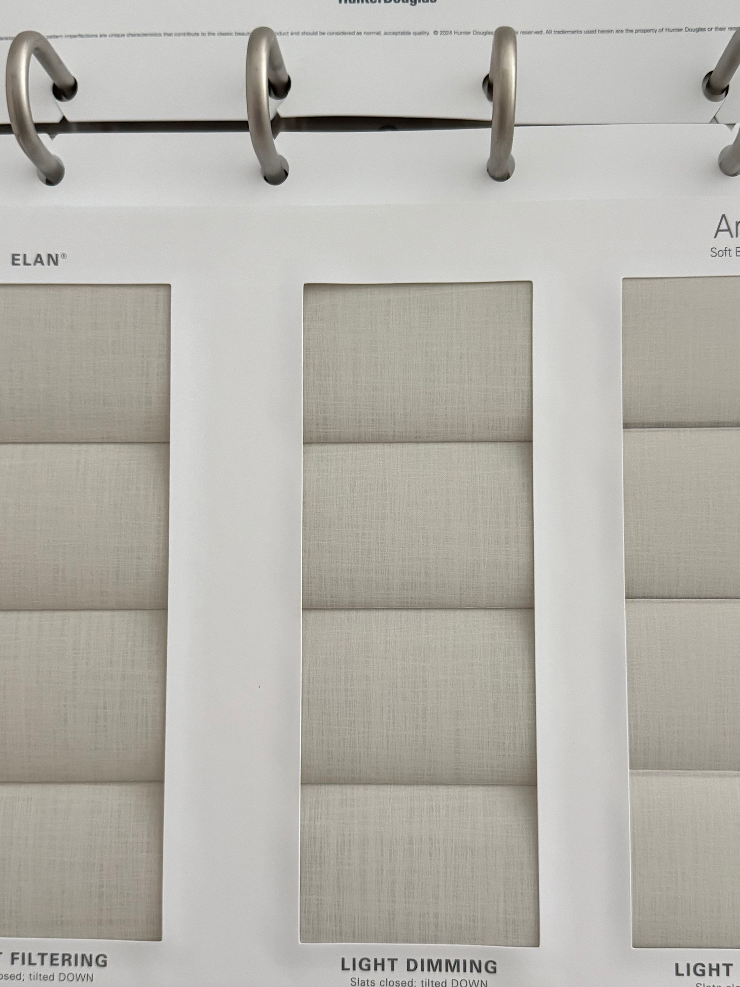 Close-up of a binder with metal rings holding fabric swatch samples; page labeled LIGHT DIMMING shows three beige fabric panels.