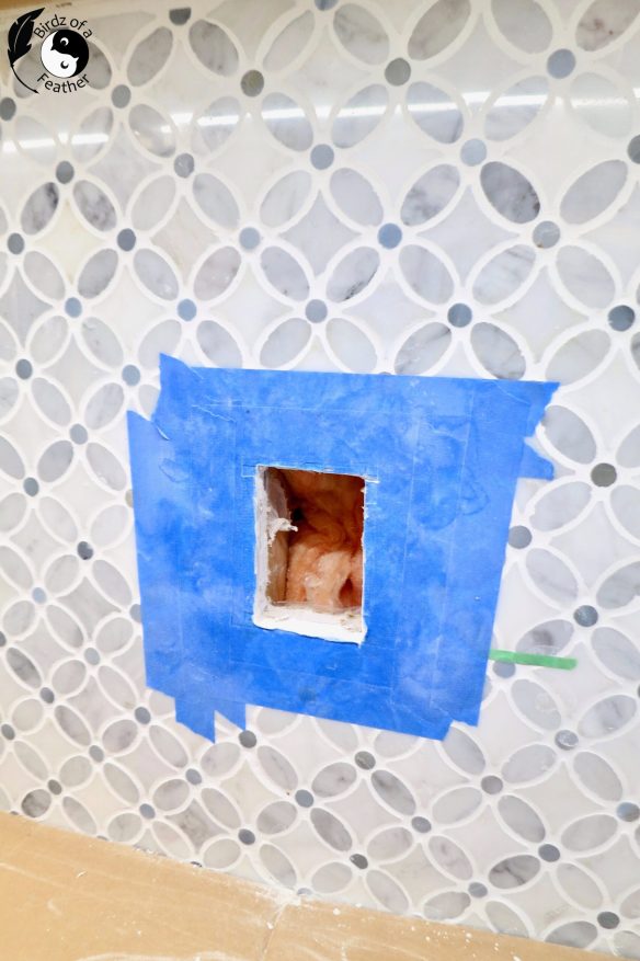 Hole cut into the tile surrounded by blue painters tape to add an outlet