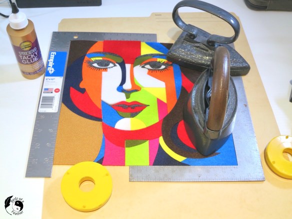 DIY abstract art between two 90 degree rulers with iron weights on top and a bottle of Aleene's glue beside it