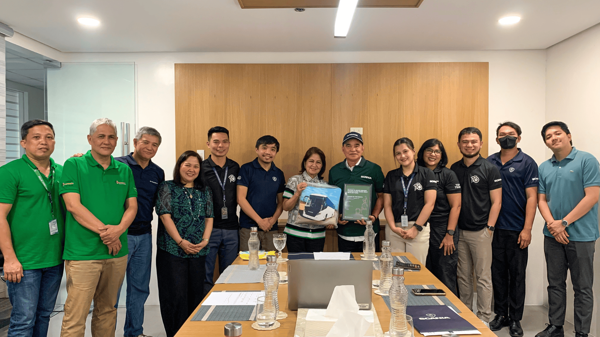 BJM Mercantile and Scania representatives gathered around a conference table presenting the Scania A Good Driver July 2026 award plaque and commemorative bus pillow.