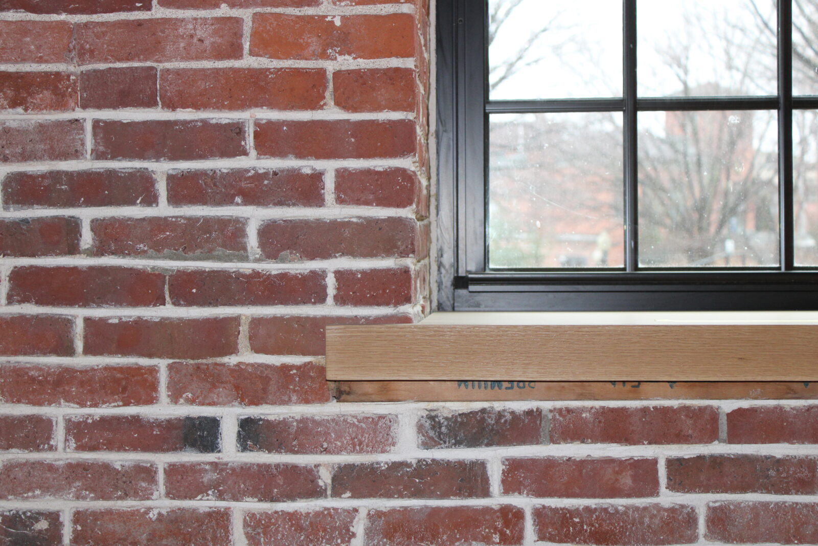 Brick wall with a wooden window sill, featuring a black-framed window, showcasing the Industrial History Center's architectural design and historical elements.
