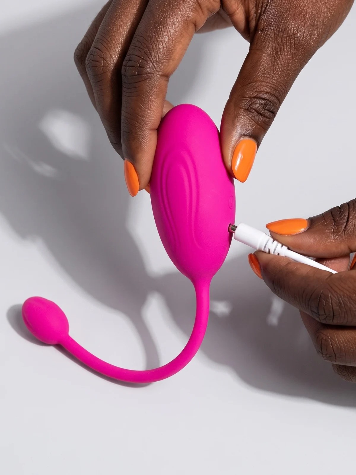 Lover Link rechargeable pink wearable vibrator held in hands while connecting its charging cable.