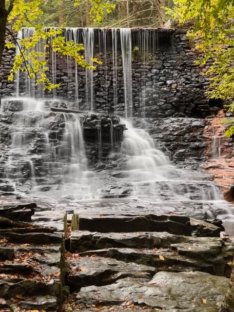 Cascading waterfall flowing over a stone dam and rocky ledges surrounded by forest at Hickory Run State Park in Pennsylvania.