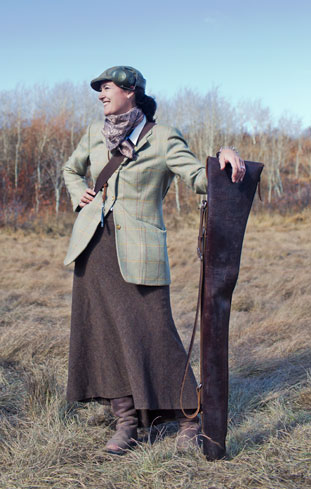 Jen Magnusson in a tweed jacket and long skirt holding a gun slip in a field