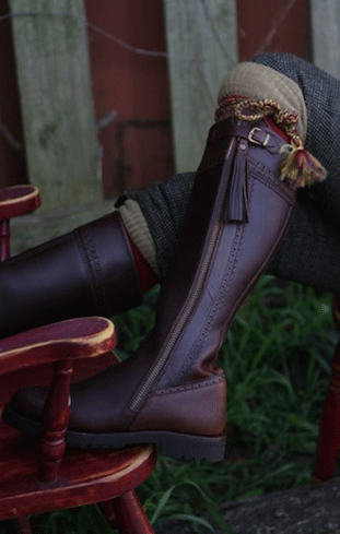 Leather field boots with buckle straps beside a wooden fence