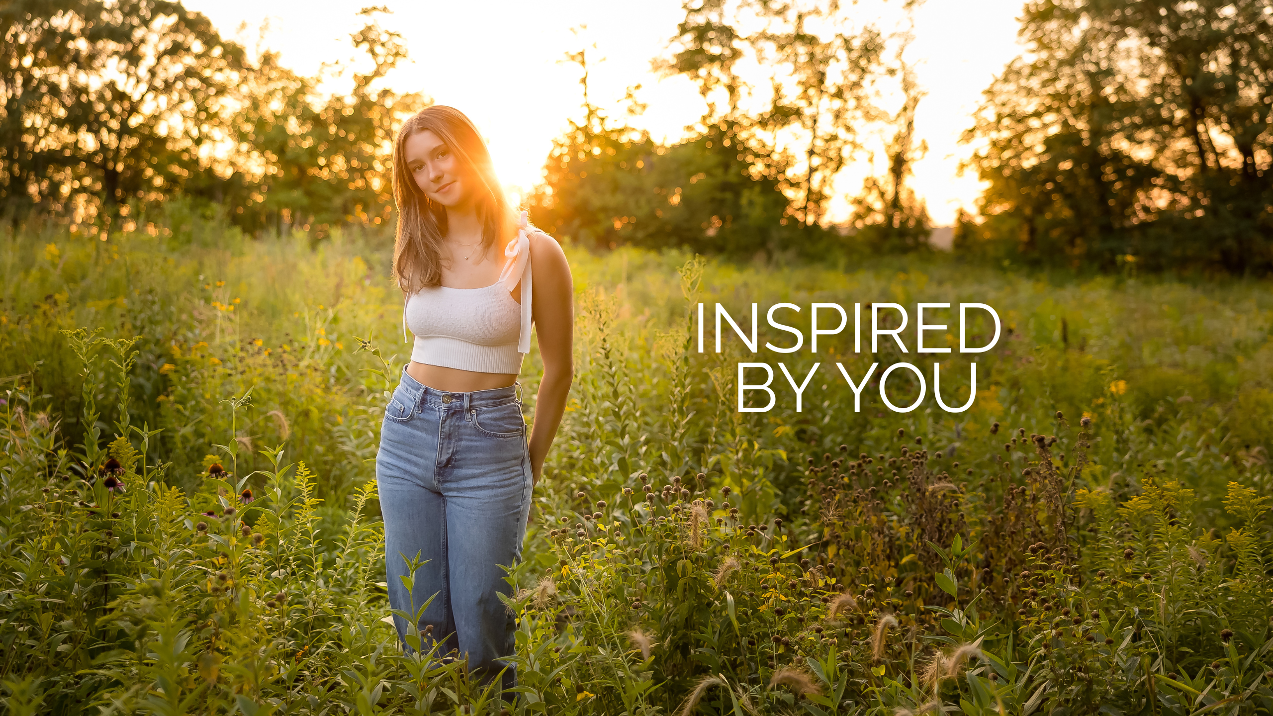 Sunset grassy field with high school senior girl wearing jeans and a white crop top. Text says "Inspired by You."