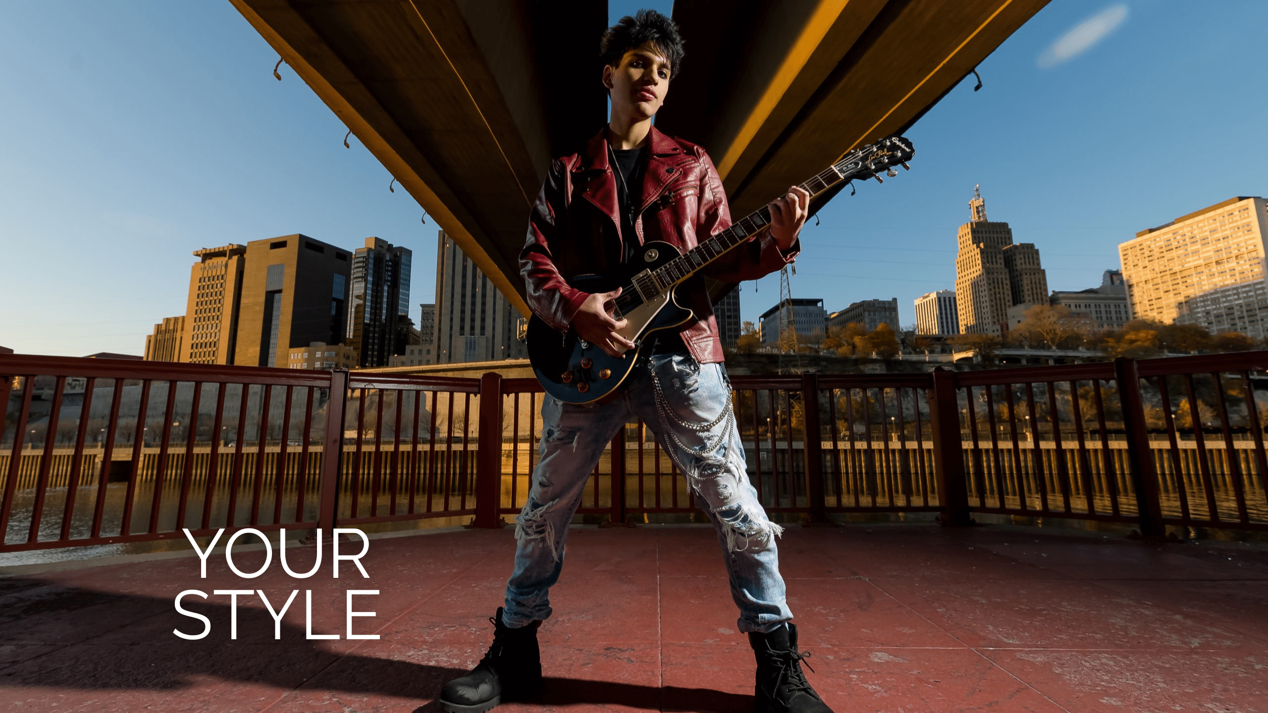 Wabasha Bridge in St. Paul with high school senior male wearing torn jeans, a red leather jacket, and combat boots holding an electric guitar. Text says "Your Style."