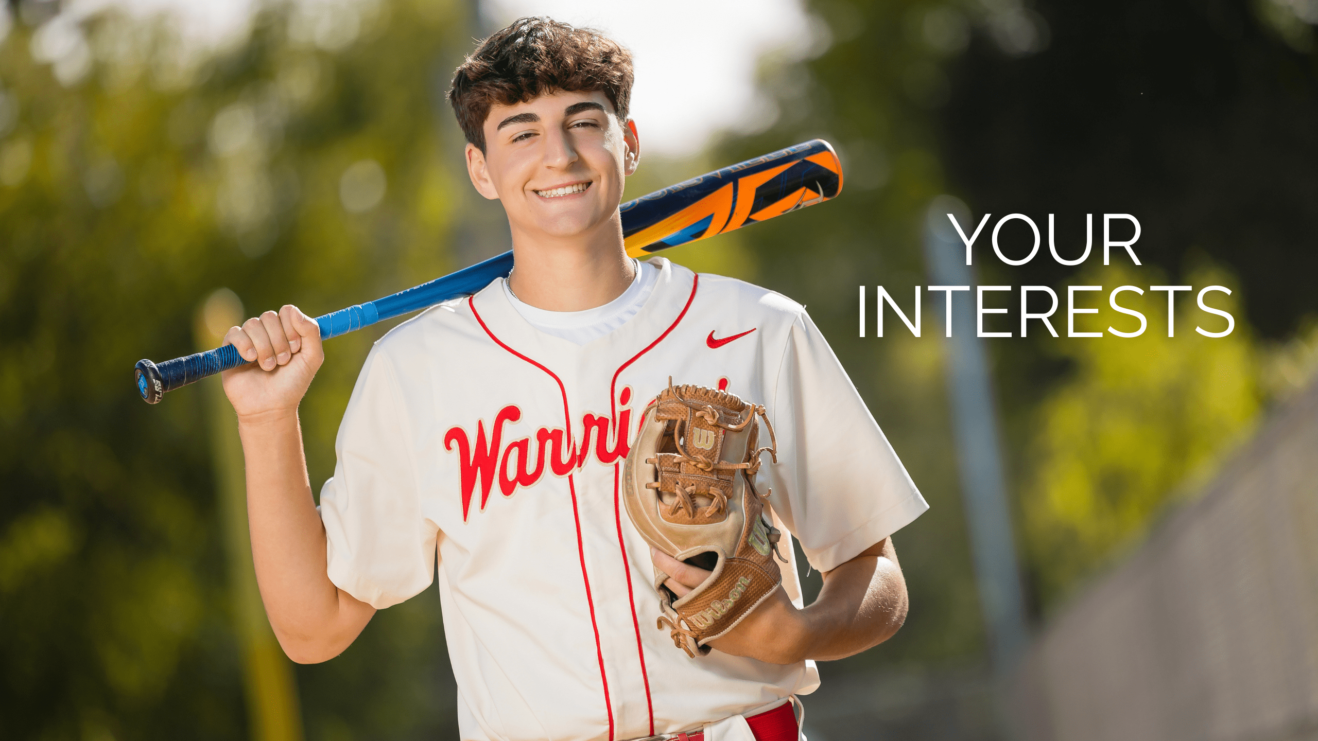Baseball high school senior portraits with male wearing white and red baseball uniform holding a baseball bat and glove on a baseball field. Text says "Your interests."