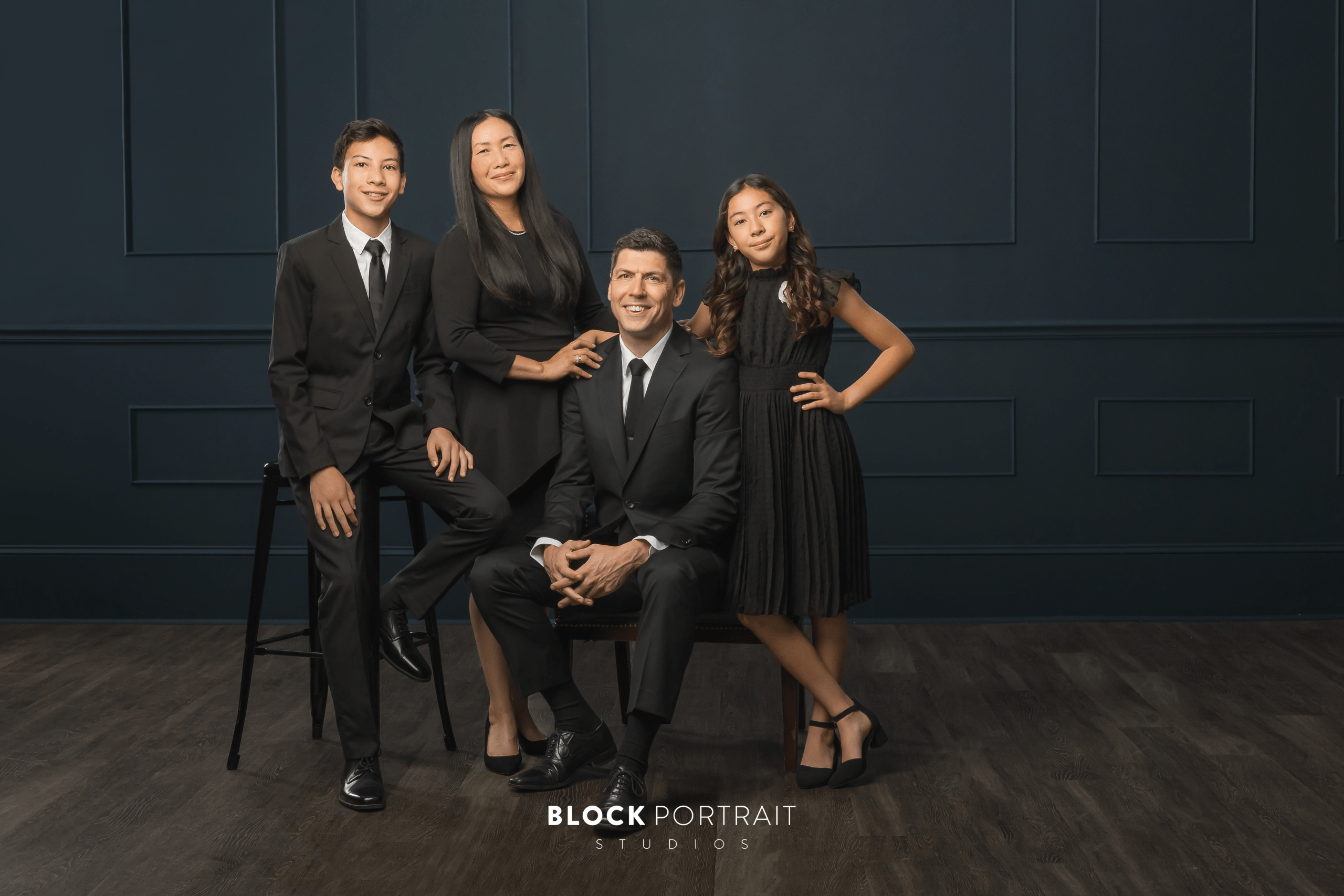 A family of four wearing black formalwear with the dad and son in suits and the daughter and mom in black knee-length dresses.