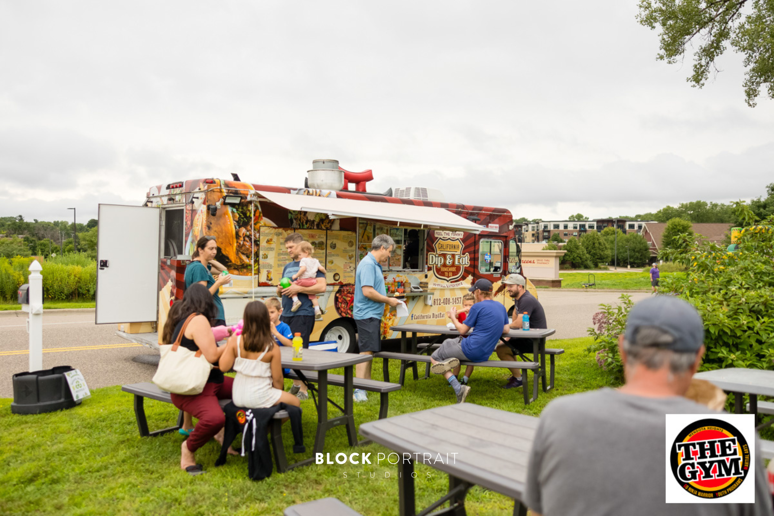A food truck with picnic tables and people sitting down to eat.