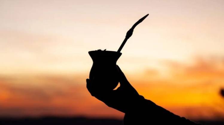 Mão segurando cuia de chimarrão ao pôr do sol, símbolo da cultura gaúcha. Chimarrão ao pôr do sol — tradição gaúcha