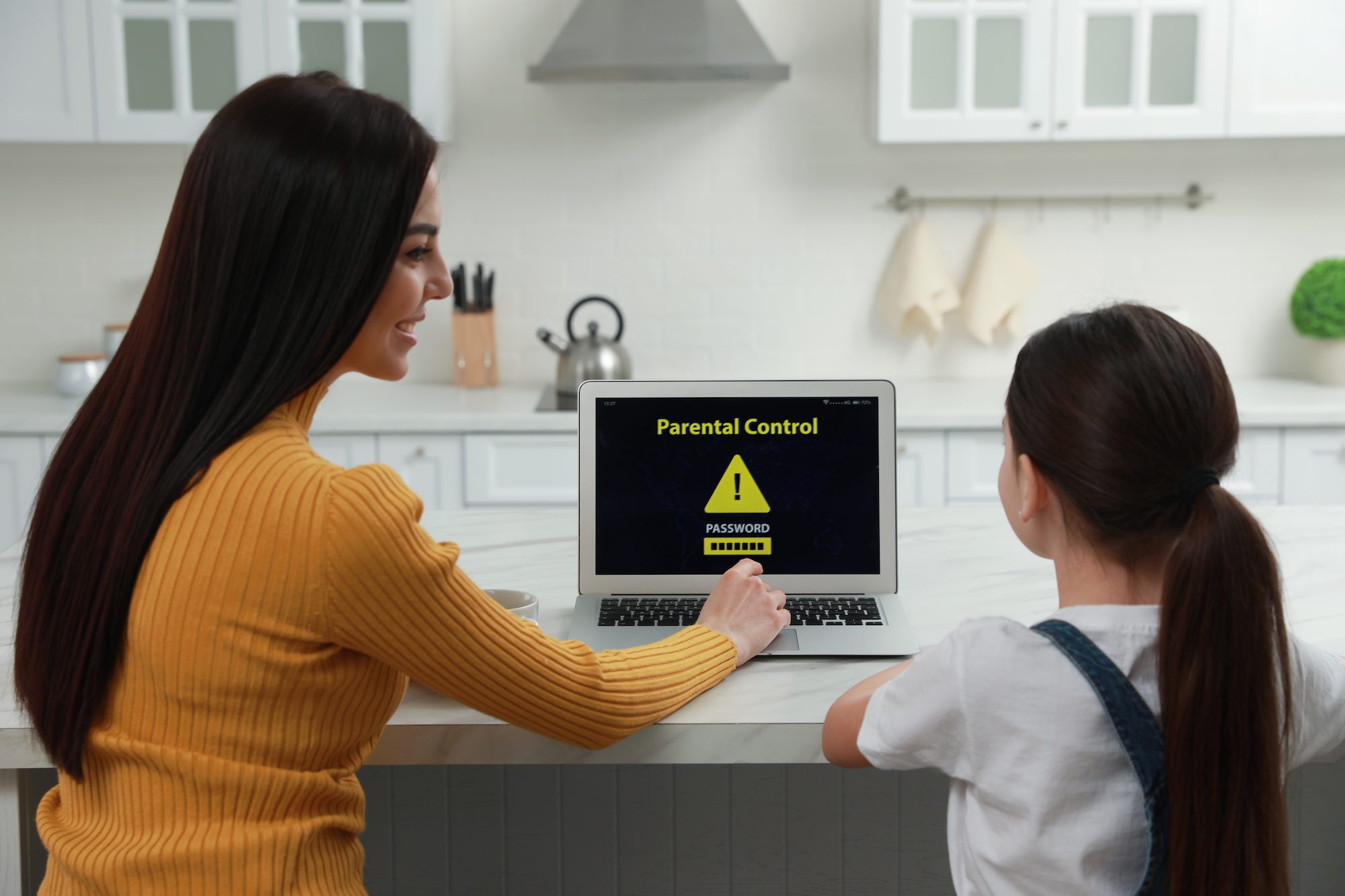 Mother installing parental control on laptop in kitchen, back view.