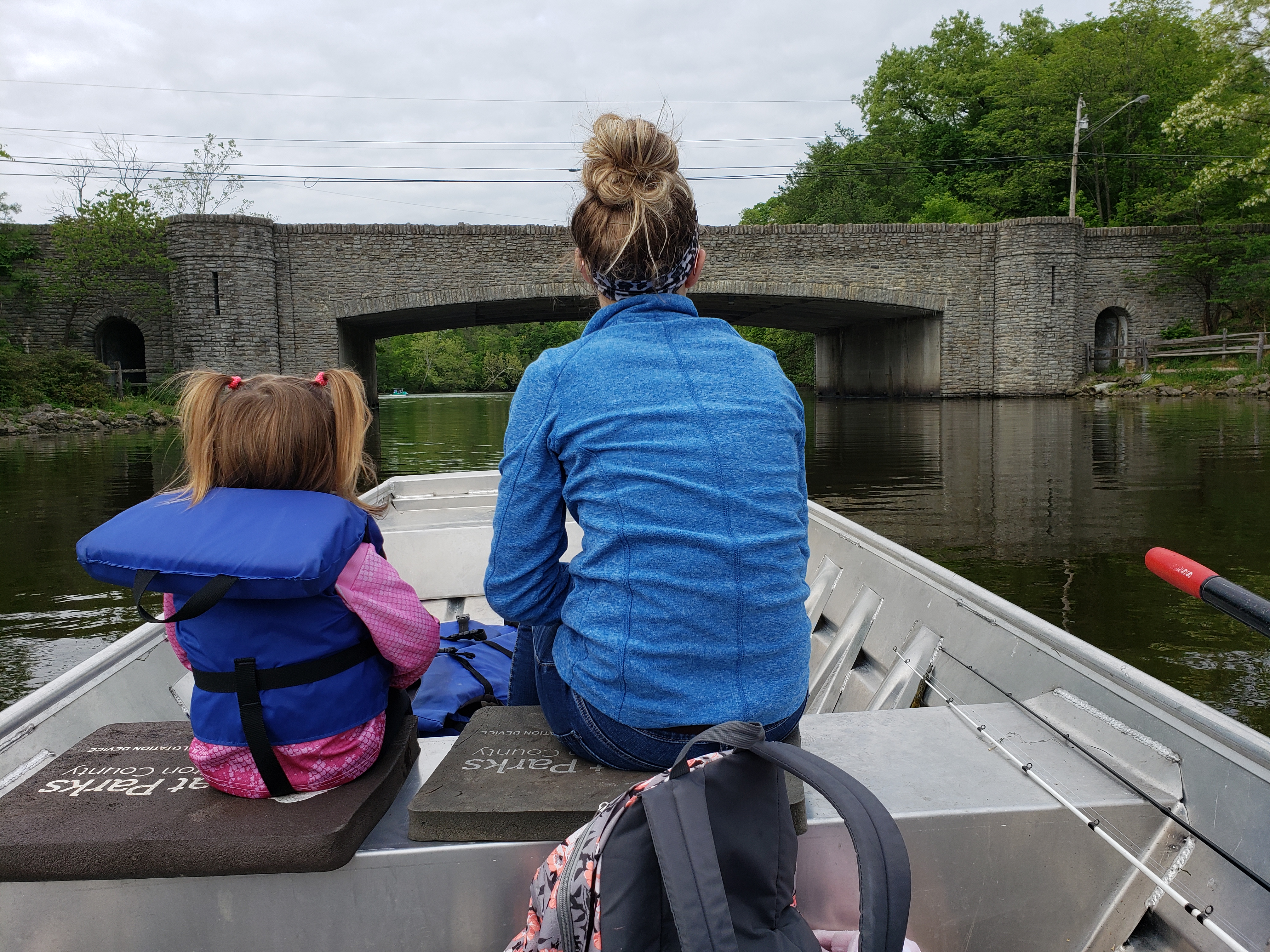 Adilyn and a woman sit in a fishing boat at Sharon Lake. They are facing toward the front of the boat and photo is taken from the back.