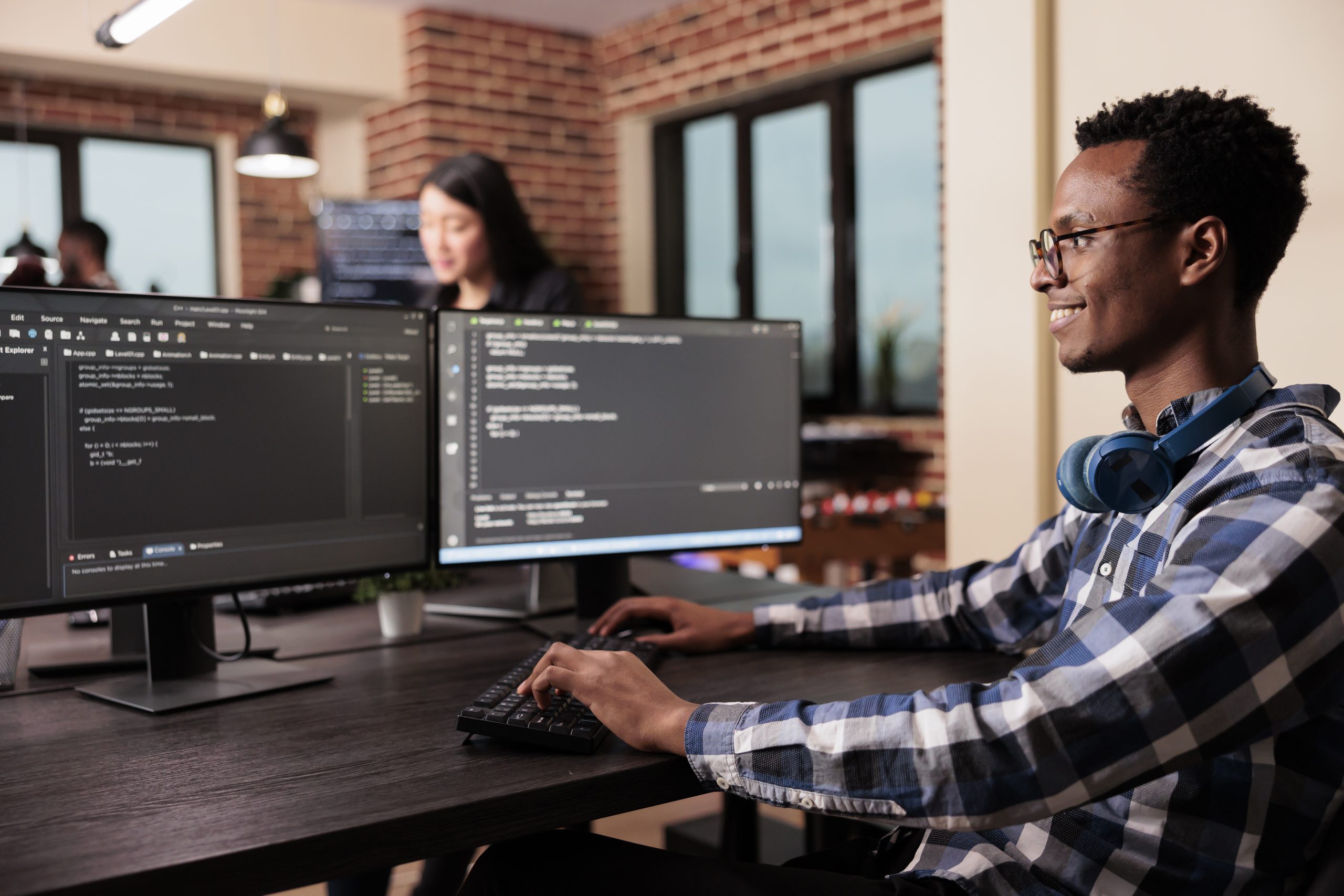 Profissional de TI utilizando computador, com dois monitores mostrando linguagem de programação.