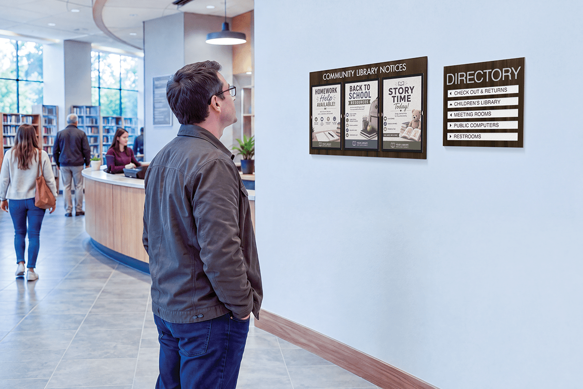 A visitor reads a Botanica 5-line directory and announcement board in a modern public library lobby.