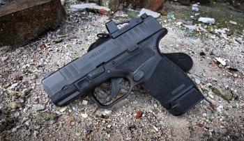 Springfield Hellcat pistol with red dot optic and industrial background in the dirt