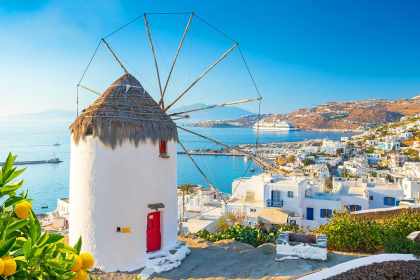 10 Best Beach Clubs & Bars in Mykonos, Greece: Traditional Mykonos windmill with red door overlooking whitewashed town and deep blue Aegean Sea under clear sky