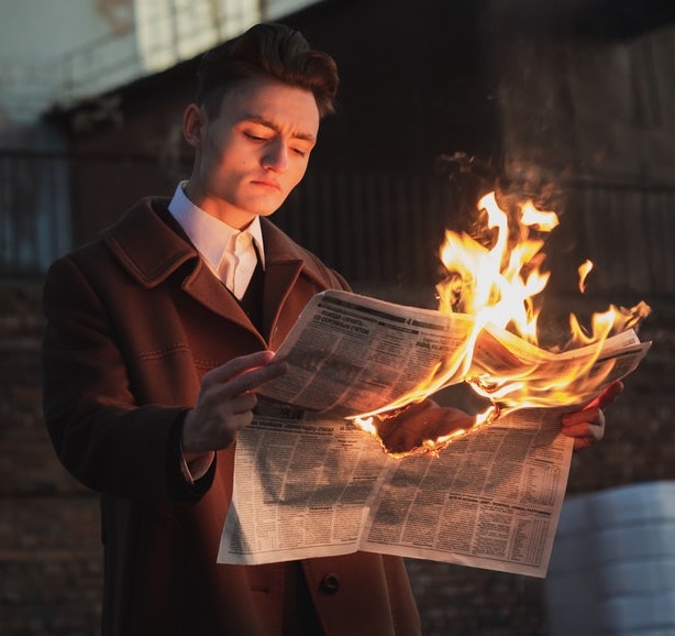 A young man reads a burning newspaper