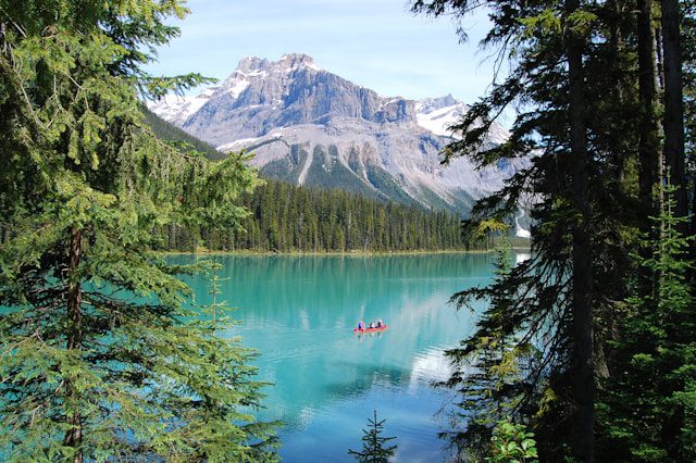 Emerald Lake in Canadian Rockies with turquoise water, red canoe, surrounding pine forest and mountain backdrop.