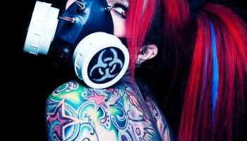 tattooed woman in red hair wearing gas mask while looking afar