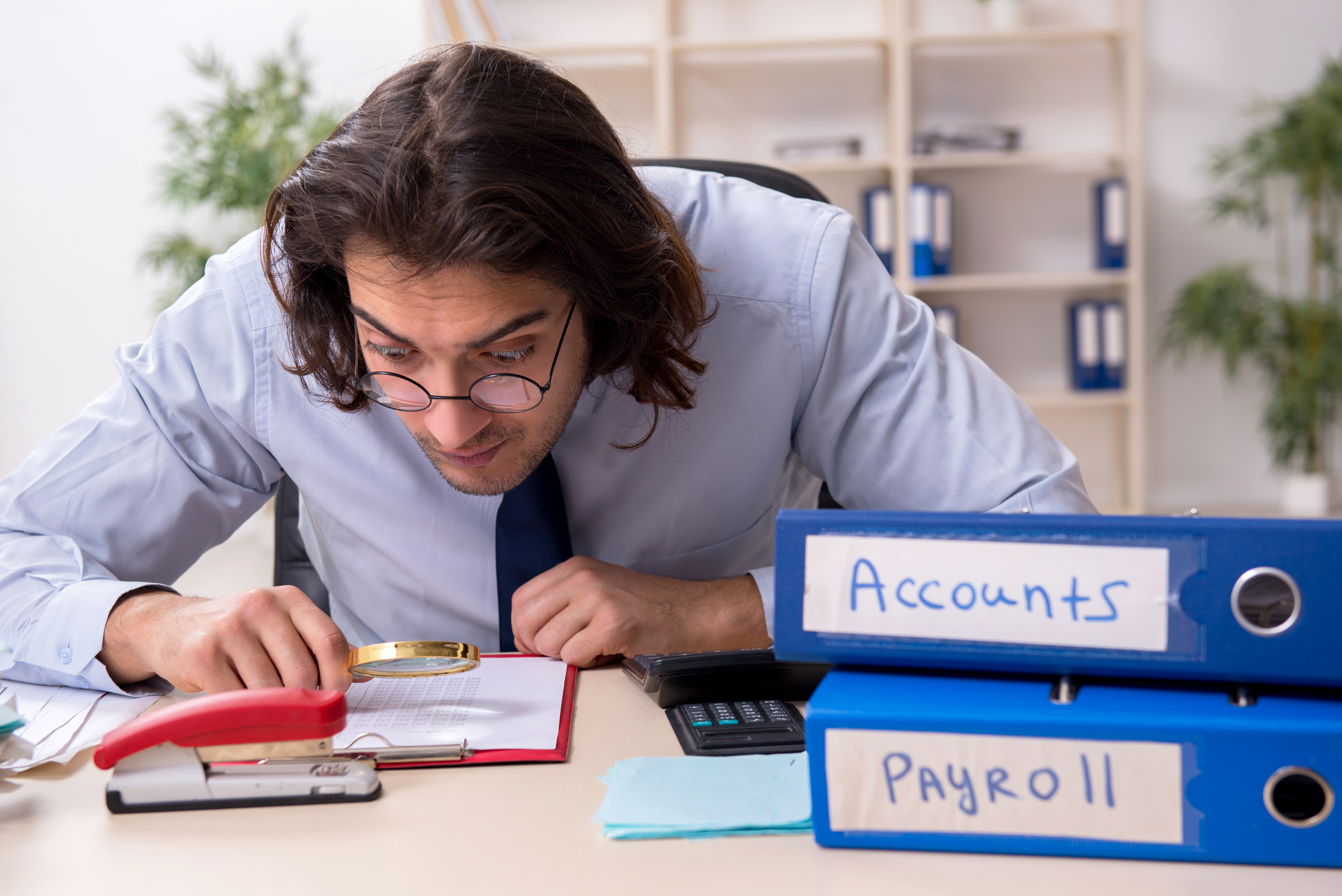 Business owner finding payroll mistakes with a magnifying glass on the books.