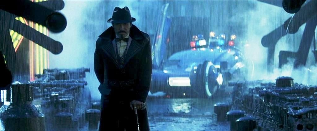Edward James Olmos as Gaff standing next to a police spinner in the rain, showcasing the visual detail defined during Ridley Scott's pre-production process.