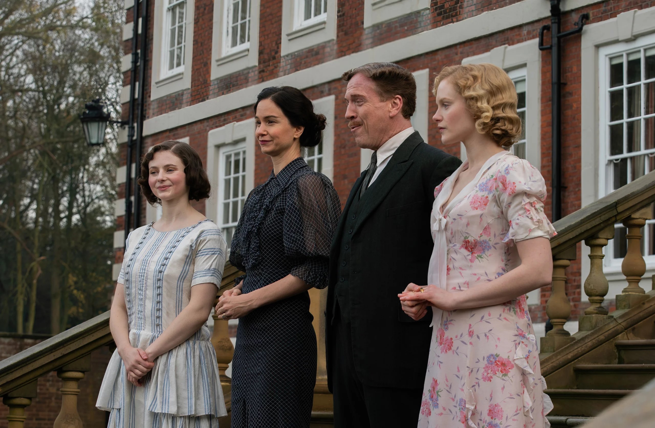 Thomasin McKenzie, Katherine Waterston, Damian Lewis, and cast members standing on the steps of a grand estate in the 2025 period comedy Fackham Hall.