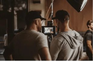 Two students using film production software for students to review footage on a camera monitor during a media class project.