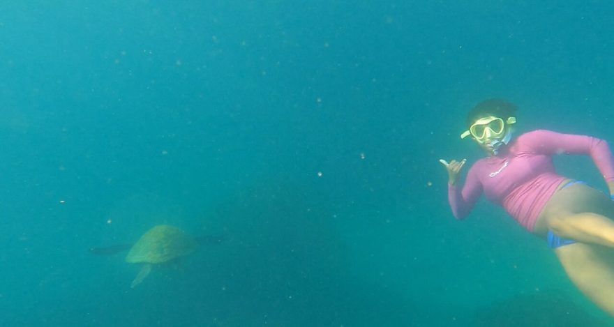 Roseline Gragg in a snorkeling mask swimming next to a green sea turtle underwater.
