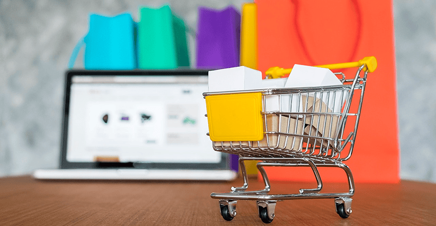 Mini carrinho de compras com sacolas dentro, na frente de um notebook aberto em um e-commerce
