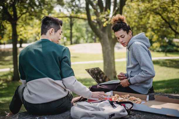 two students sitting in a park eating pizza