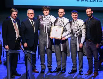 London Parade Invitation-23 Representatives from the London Parade office and the city of London talk Wednesday, March 22, 2023 in the Hayes Concert Hall while presenting the Marching Mocs with their official invitation to participate in the London New Year’s Day Parade. Left to right: Senior Patron Duncan Sandys, former Lord Mayor of the City of Westminster, Randall Coleman, director of bands, band members Justin Haynes, Matthew Warren and Dylan Campbell, and Robert Truan, assistant director of bands.