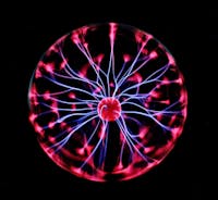 Close-up of a plasma globe with vibrant neon sparks against a dark background.