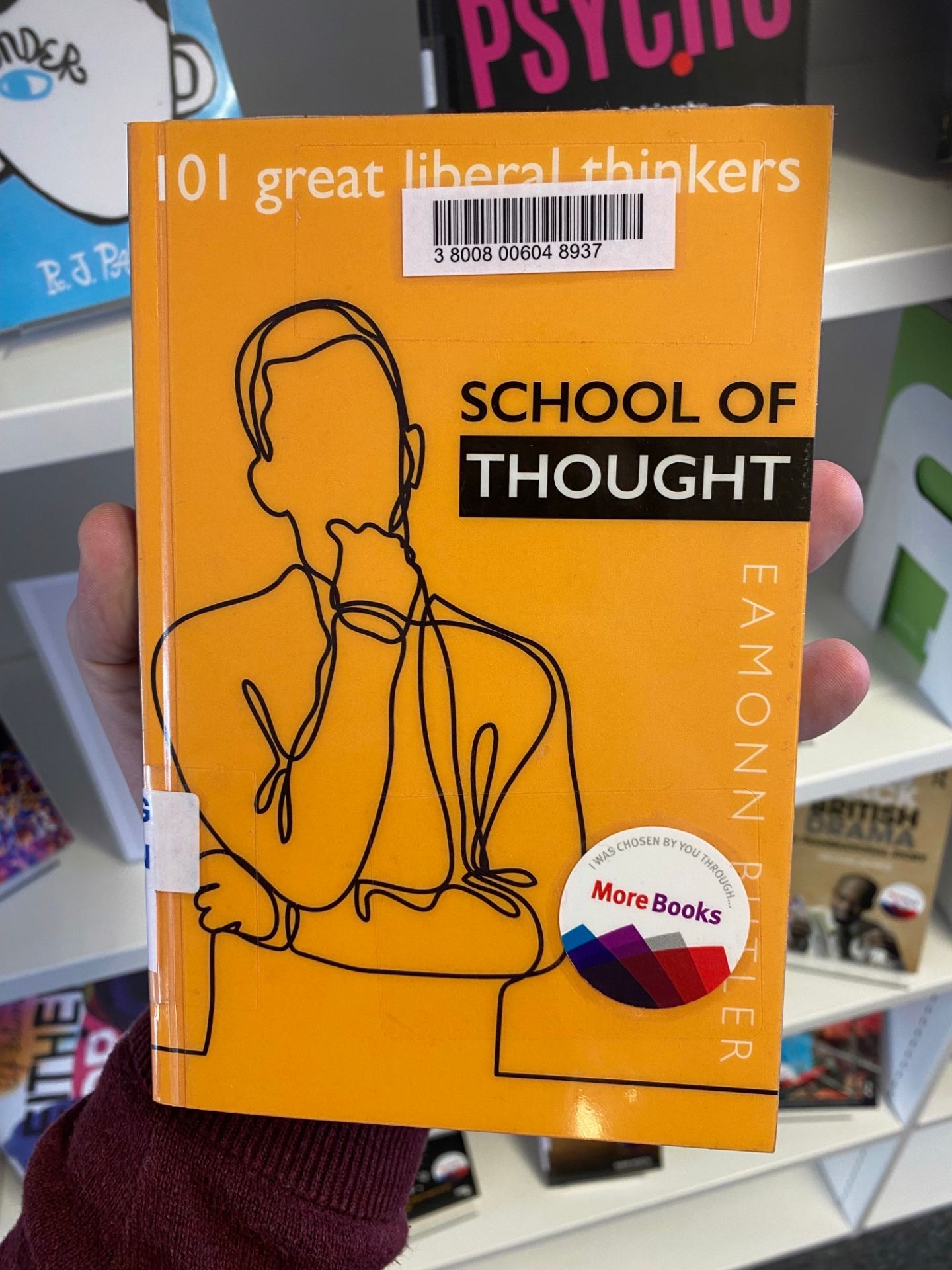 A hand is holding a book entitled School of Thought: 101 Great Liberal Thinkers, by Eamonn Butler. The book has a "More Books" sticker on the cover.
