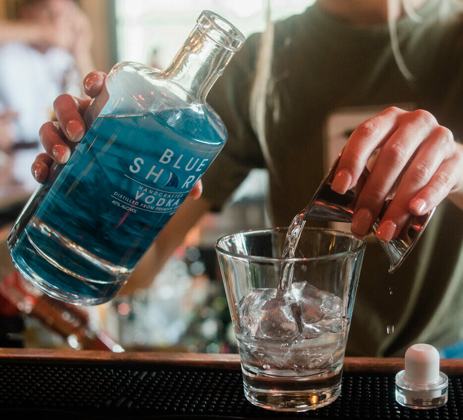 A bartender pours a shot of blue shark vodka